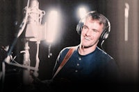 a man smiling in front of a microphone in a recording studio